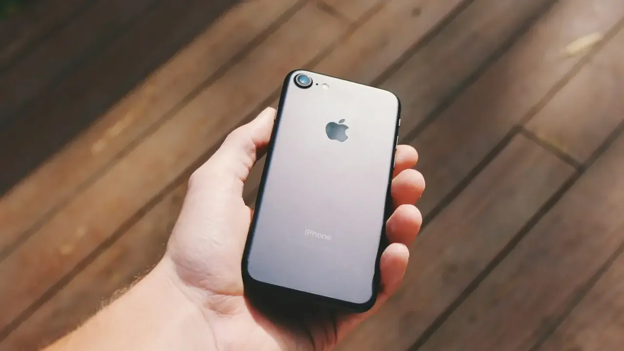 Dłoń trzyma szarego iPhone'a. Chcesz wiedzieć, jak sprawdzić, czy iPhone jest oryginalny? Zwróć uwagę na detale.
