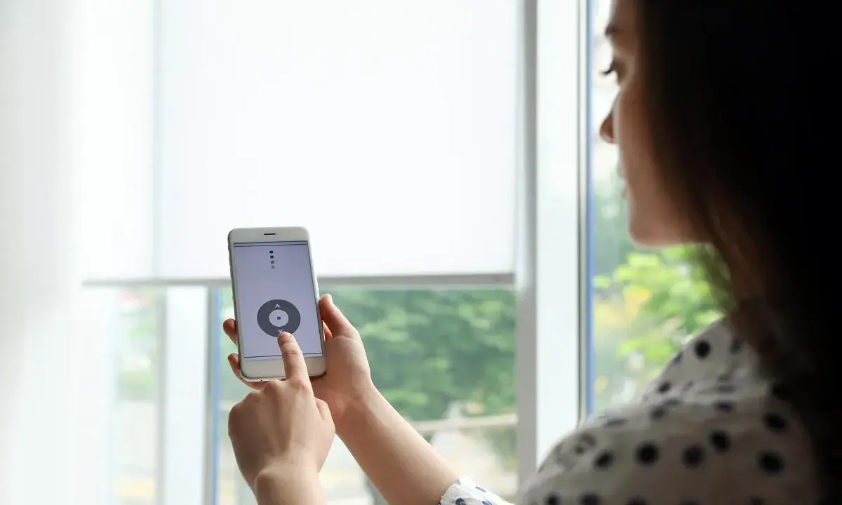 Kobieta steruje roletami z telefonu, dotykając ekranu smartfona.