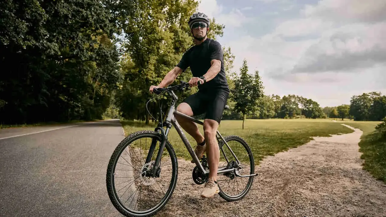 Mężczyzna w kasku i okularach jedzie na rowerze typu cross po ścieżce w parku.