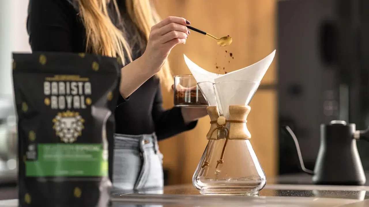 Frau bereitet Kaffee zu, um zu zeigen, was ist Caffe Latte. Kaffeepulver rieselt aus Löffel in Filter.