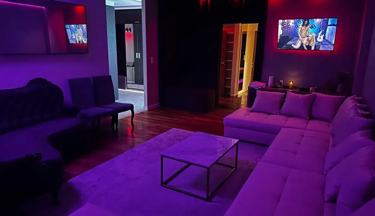 Nowoczesny salon z fioletowym oświetleniem. Na ekranie telewizora widać scenę, która może sugerować, czym jest swingowanie.