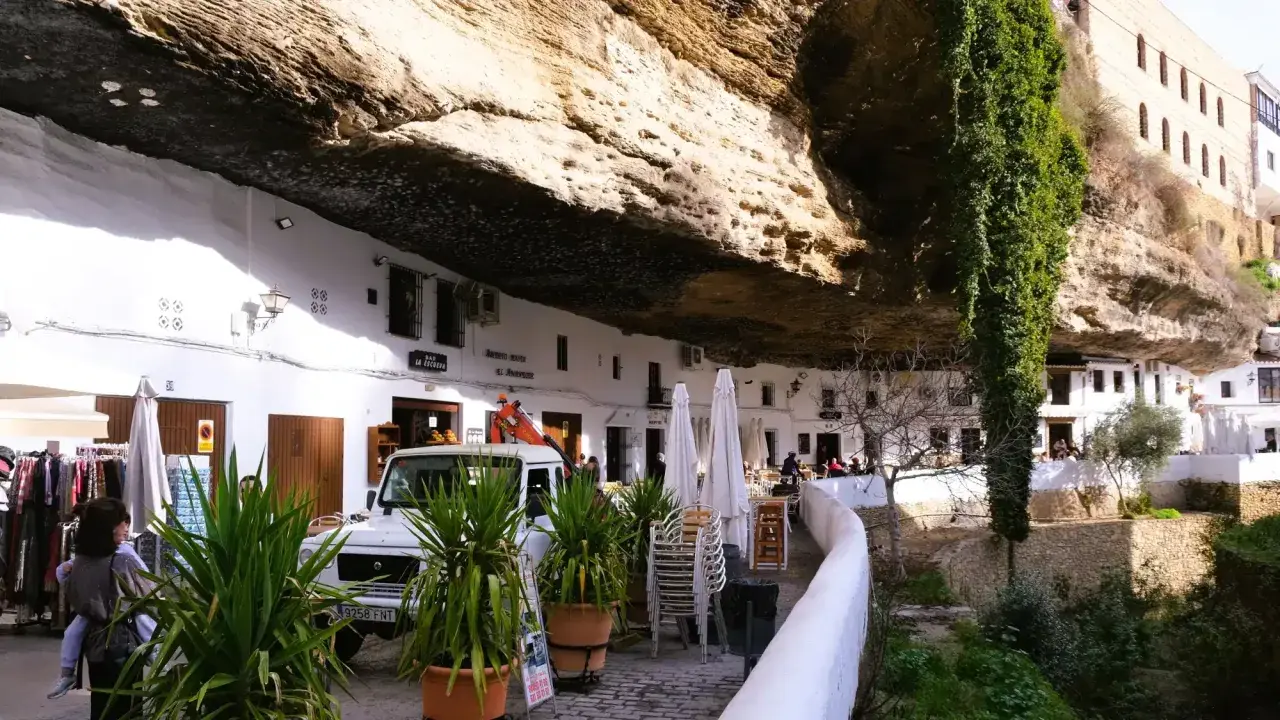 Häuser unter Felsvorsprung in Setenil de las Bodegas. Ein Auto und Pflanzen vor dem "El Gastor" Bar.