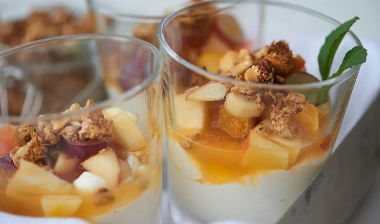 Leckeres Joghurt Dessert mit Früchten und Granola in Gläsern, garniert mit Minze.