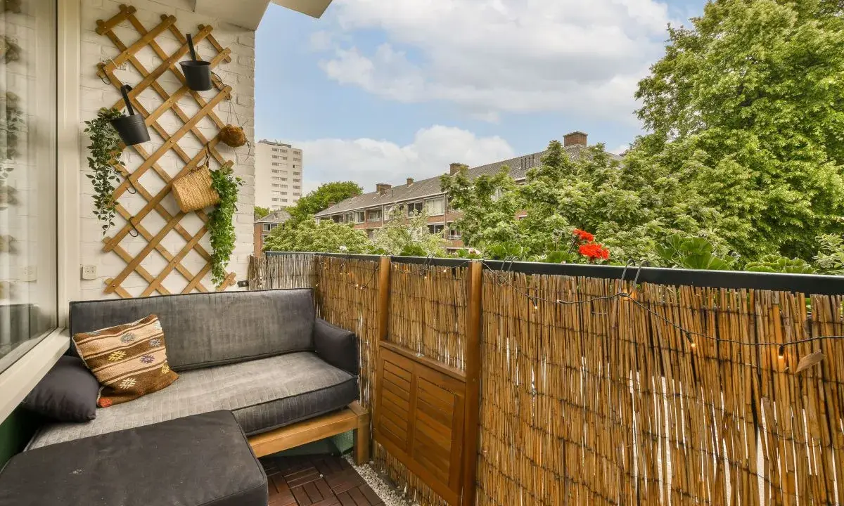 Balkon osłonięty matą bambusową, z wygodną sofą i ozdobną kratką na ścianie. Idealne miejsce, by osłonić balkon i cieszyć się prywatnością.