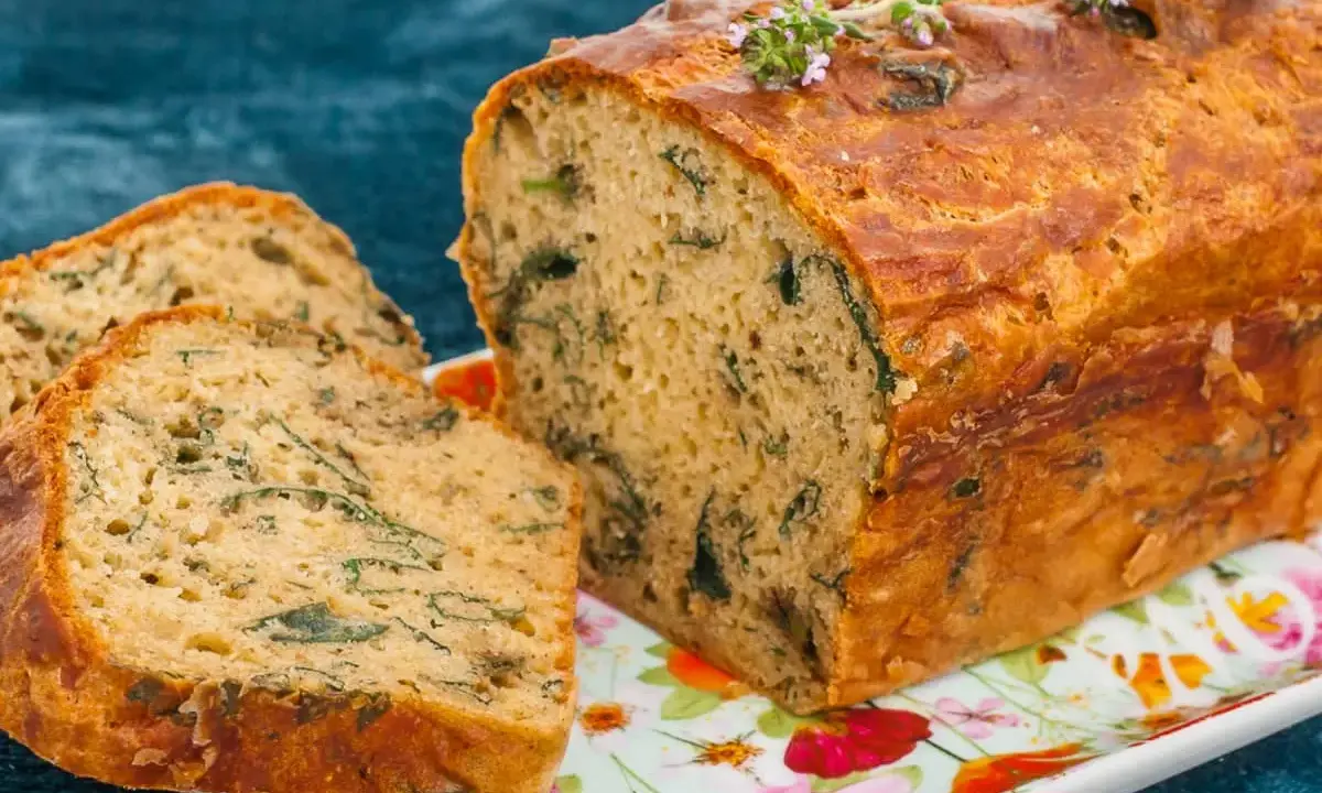 Un cake aux orties doré, garni de thym frais, est coupé en tranches sur un plat fleuri.