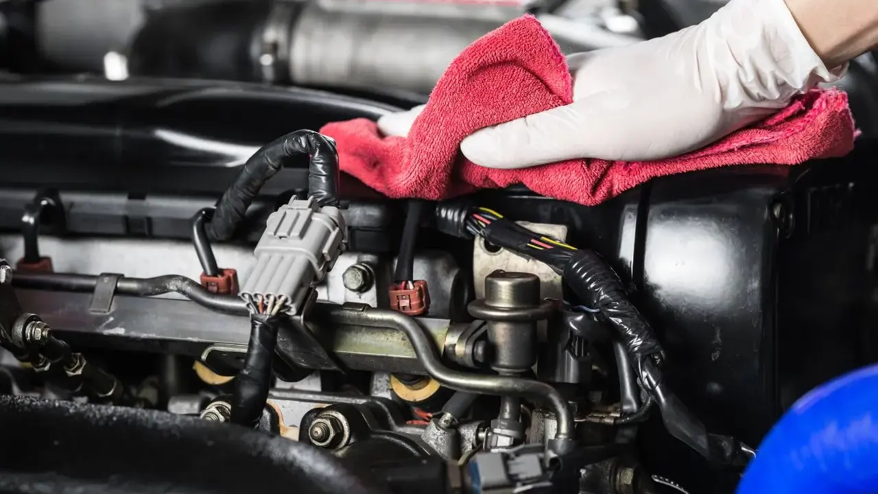 Mano enguantada realiza limpieza de piezas mecánicas de motor con paño rojo.