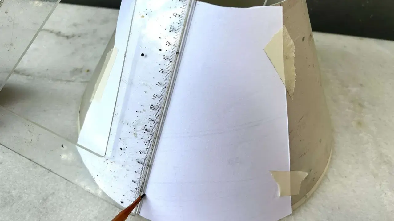 Un crayon et une règle marquent un gabarit en papier sur un abat-jour DIY.