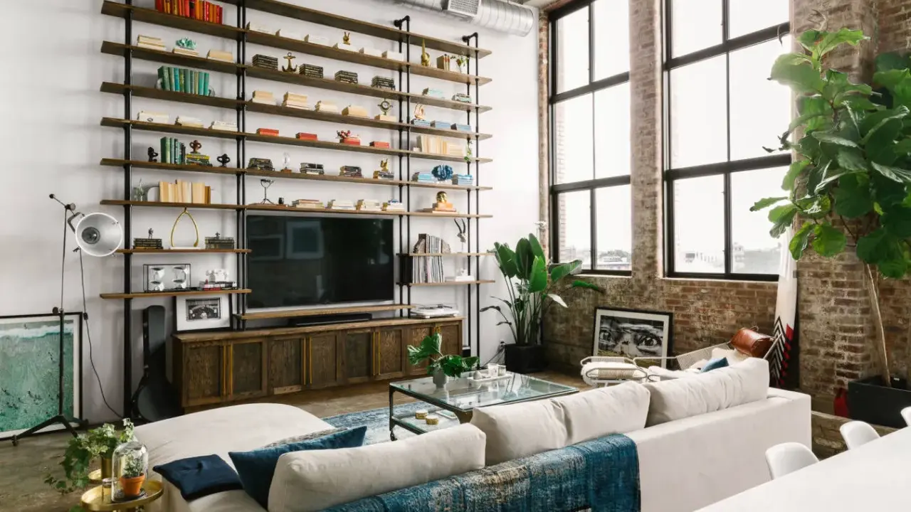 Soggiorno con scaffalatura a tutta parete, TV e divano bianco. Il soffitto alto 5 metri crea un'atmosfera ariosa, accentuata dalle grandi finestre.