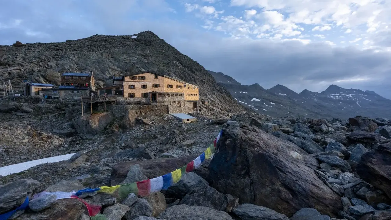 Rifugio alpino nel **parco naturale gruppo di Tessa**, con bandiere di preghiera colorate che ondeggiano tra le rocce.