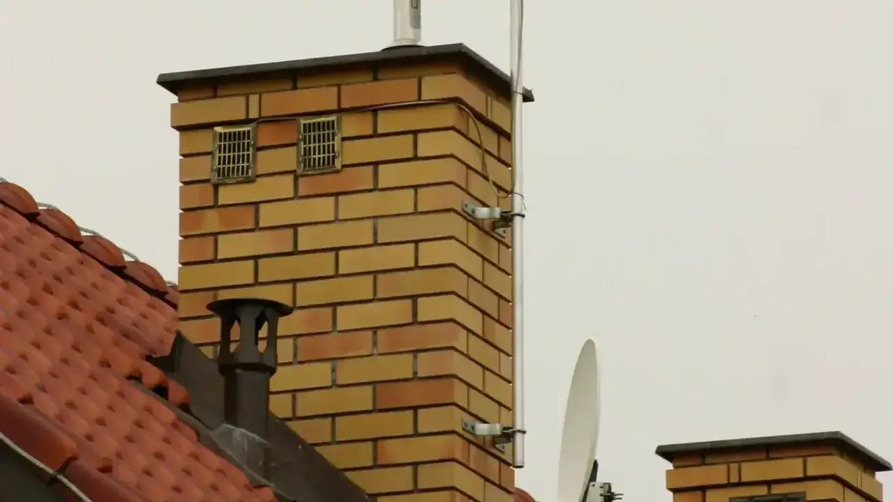 Dwa kratkowane otwory wentylacyjne na ceglanym kominie, zapewniające prawidłowe odpowietrzenie pionu sanitarnego zgodnie z normą.