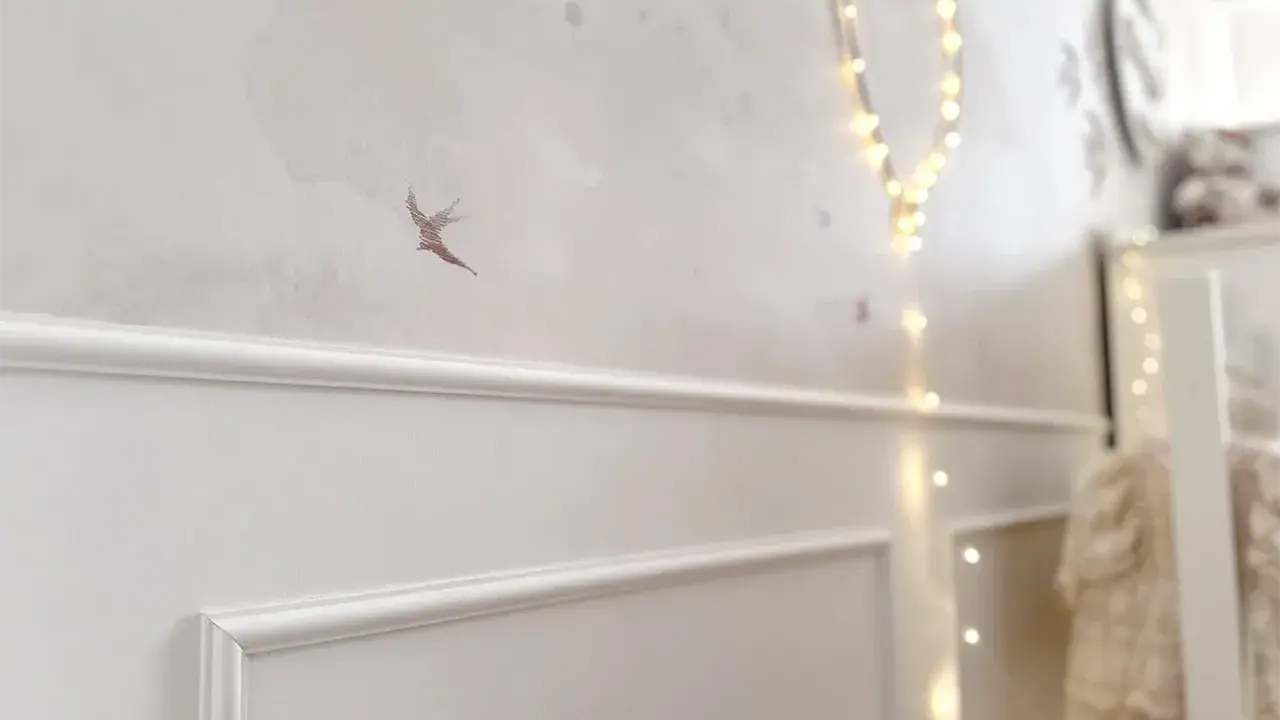 Elegancka sztukateria na ścianie w pokoju dziecka, ozdobiona motywem ptaszka i migoczącymi lampkami.