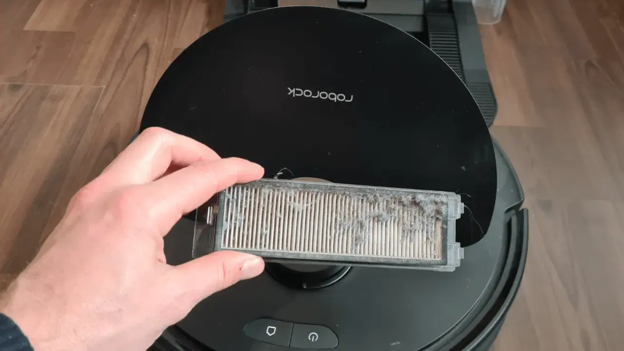 Hand hält einen stark verschmutzten Staubfilter eines Roborock Saugroboters, bereit für die Reinigung.