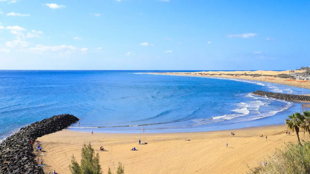 Sonniger Strand auf Gran Canaria mit goldenem Sand, türkisfarbenem Meer und einigen Menschen, die die Sonne genießen.