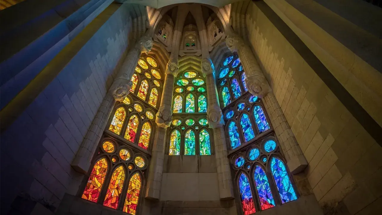 Ventanas de vidrieras de colores vibrantes, que narran la historia del vidrio, iluminan el interior de una catedral con tonos cálidos y fríos.