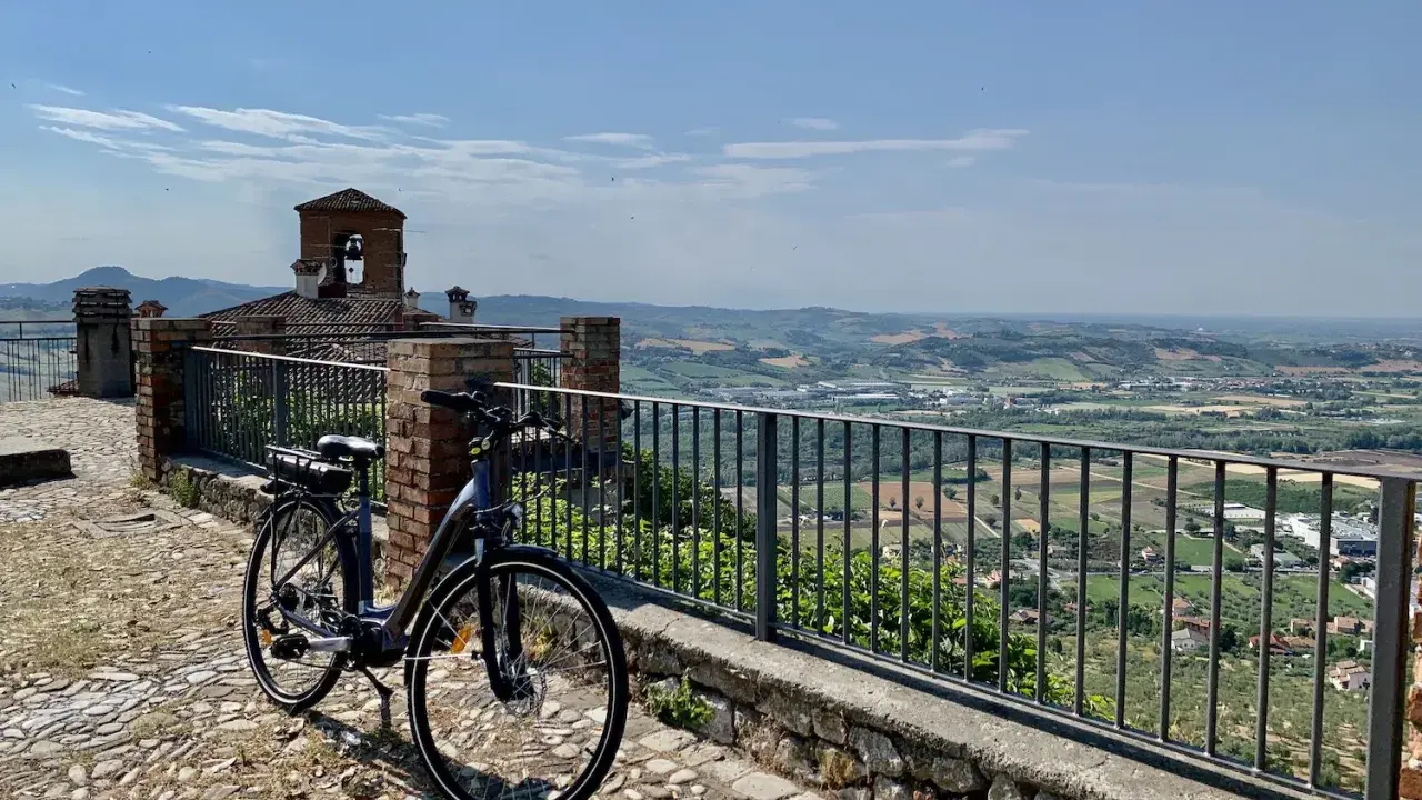 Bicicletta pronta per esplorare il **percorso fiume Marecchia**, con vista panoramica sulla valle e un antico campanile.