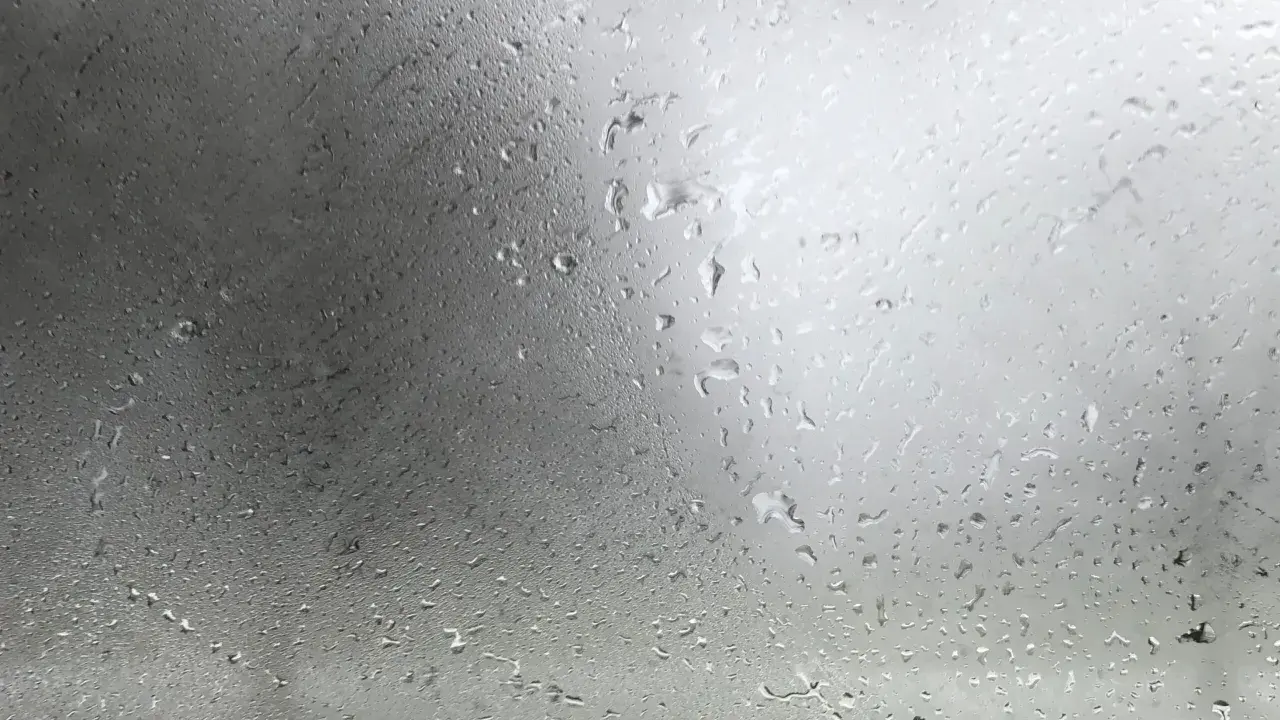 Gotas de agua sobre un cristal, reflejando un cielo nublado. La **temperatura de rocío** se siente en el aire húmedo.