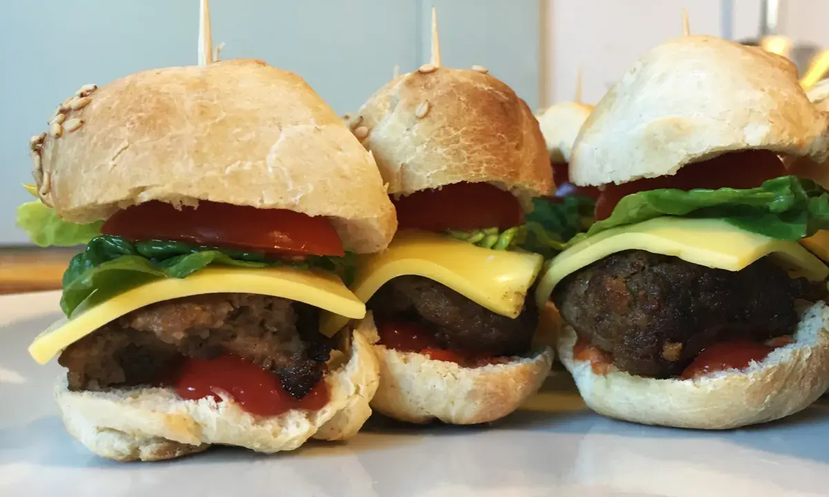 Drei leckere Slider Burger mit Käse, Tomate und Salat auf einem Teller.