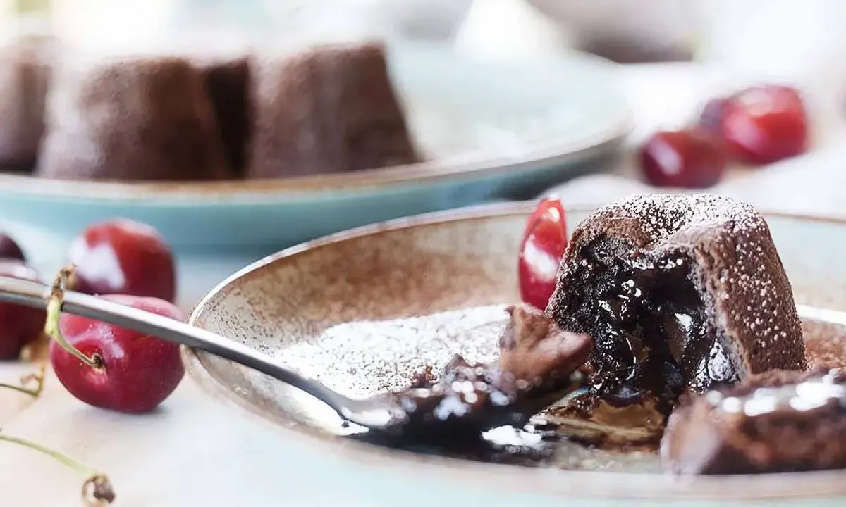 Coulant de chocolate con interior fundido, espolvoreado con azúcar glas y acompañado de cerezas frescas.