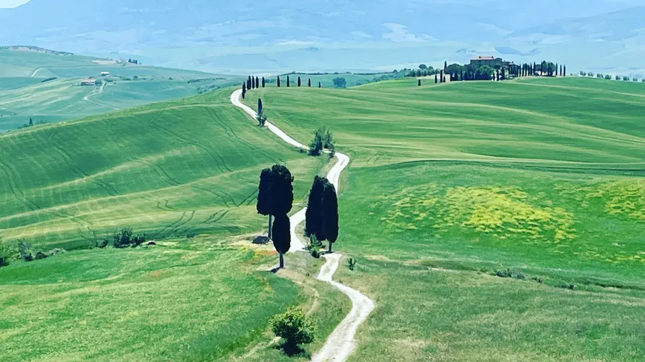 Un sentiero serpeggia tra le dolci colline verdi della Val d'Orcia, ideale per un indimenticabile trekking.