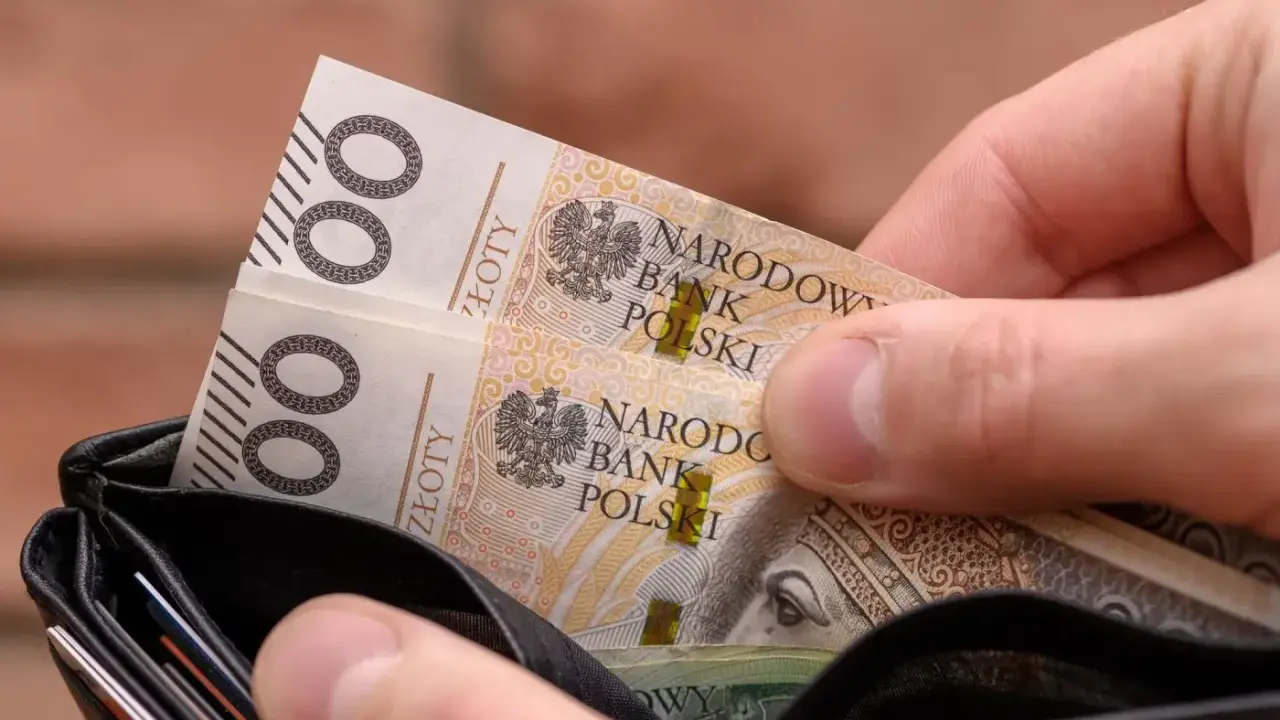 Dłoń wkłada do portfela banknoty 100 zł. Czy to na bieżące wydatki, czy może na 13. emeryturę?