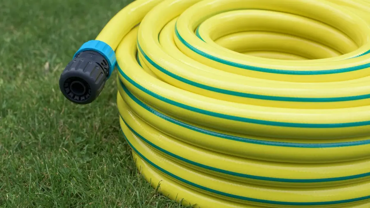 Un tuyau d'arrosage jaune enroulé sur l'herbe, avec un connecteur noir et bleu. Le diamètre du tuyau d'arrosage est visible dans son enroulement.