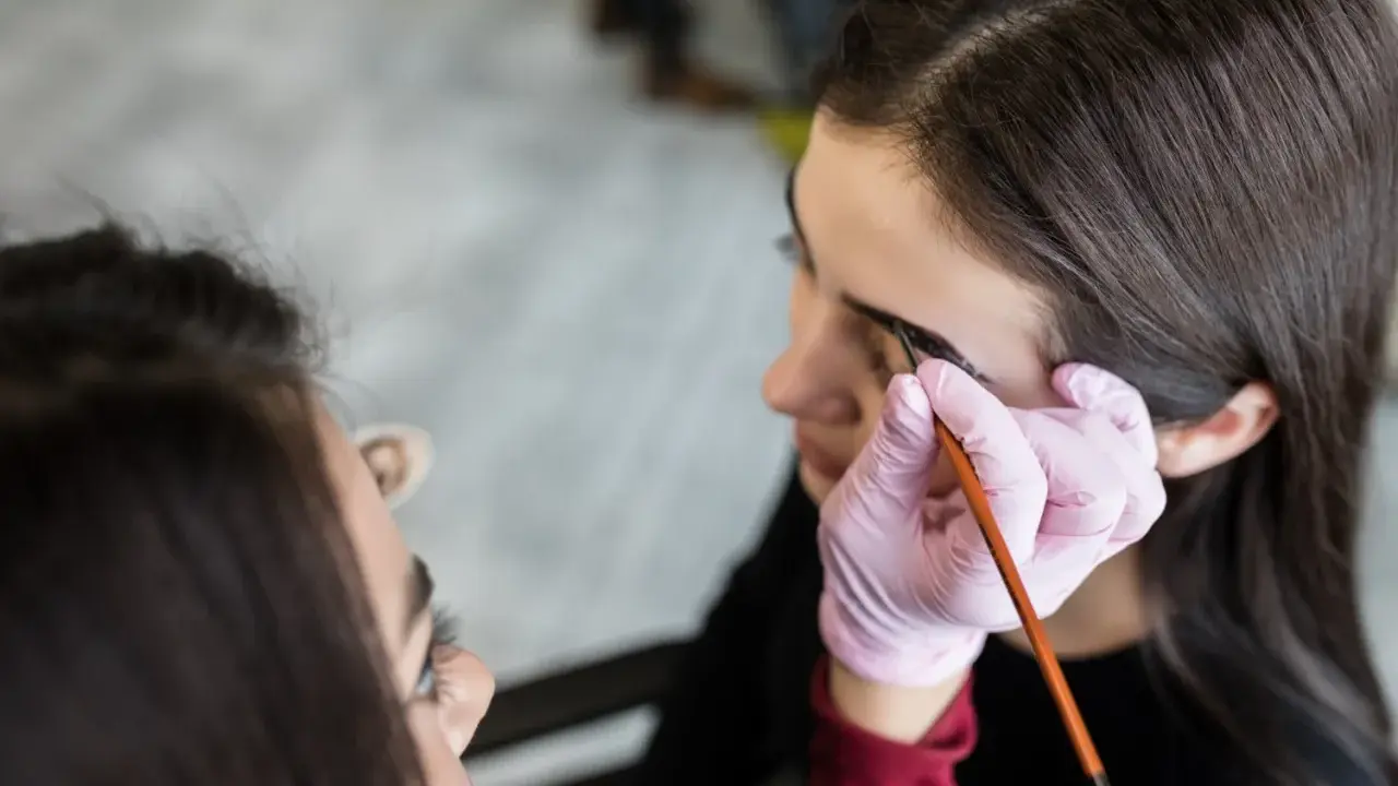 Stylistka w różowej rękawiczce aplikuje hennę pudrową na brwi klientki. Efekt naturalny, jak po hennie zwykłej, ale trwalszy.