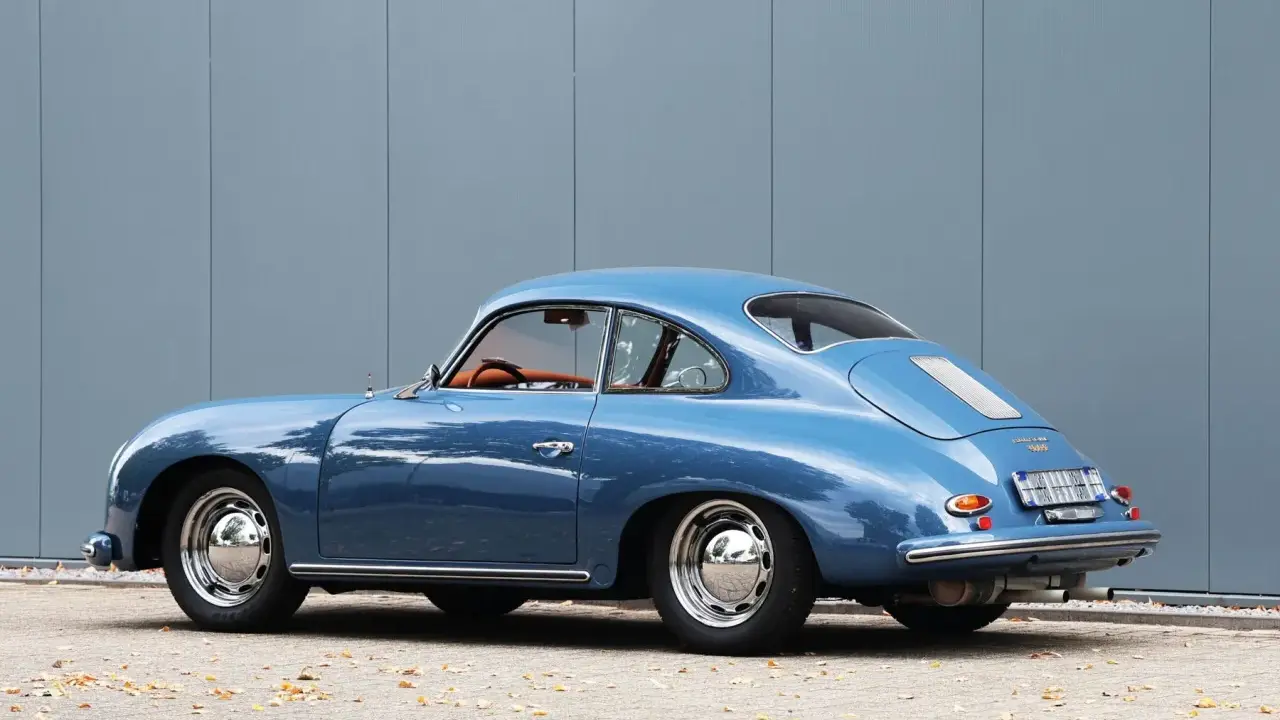 Blauer Porsche 1600 Super Coupé, ein Klassiker mit hohem Wert, steht vor einer grauen Wand.