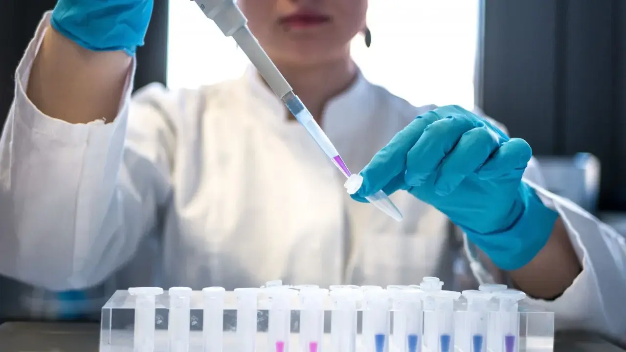 Ricerca per la terapia monoclonale: una mano guantata usa un contagocce per trasferire un liquido viola in una provetta, parte di un esperimento in laboratorio.