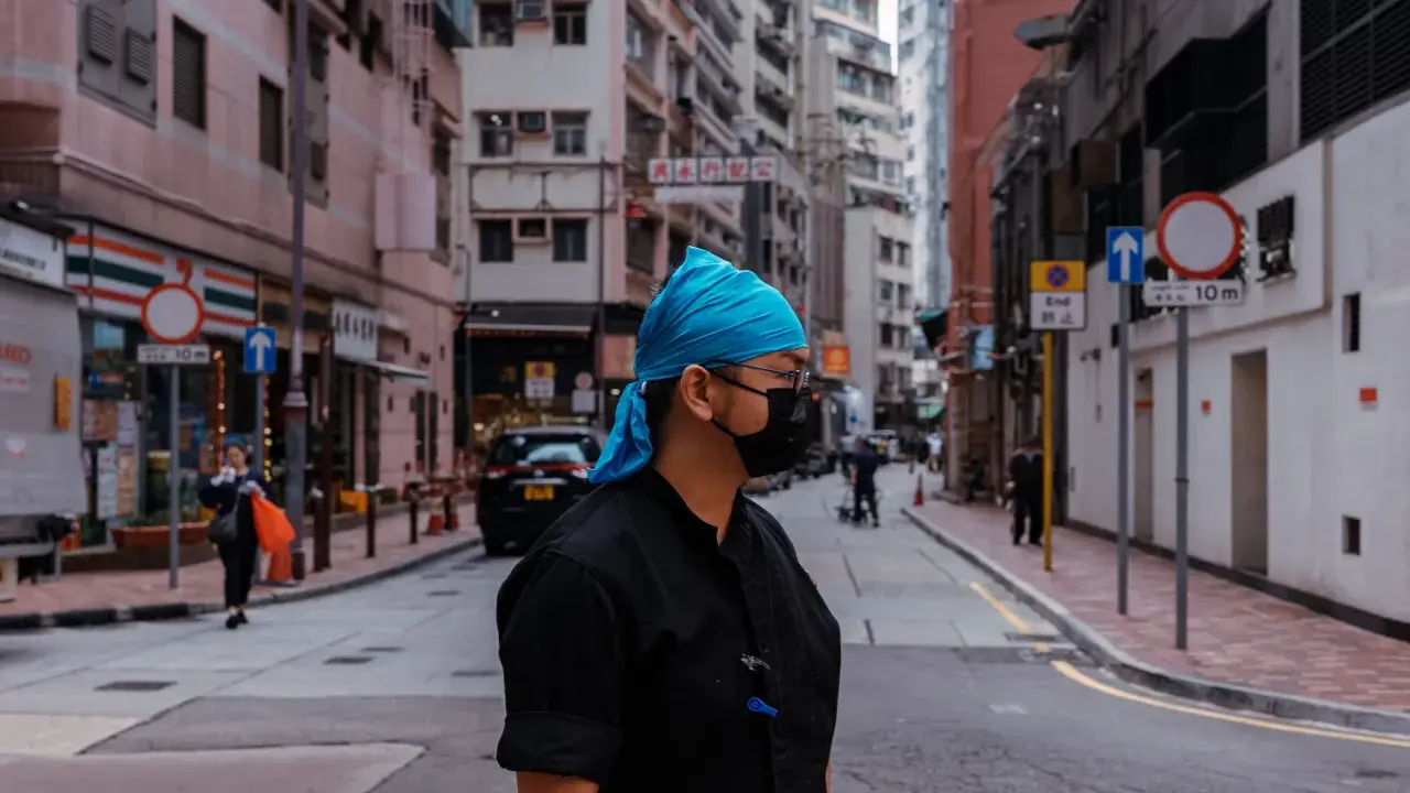 Uomo con bandana blu e mascherina nera in una foto di strada con edifici alti e traffico.