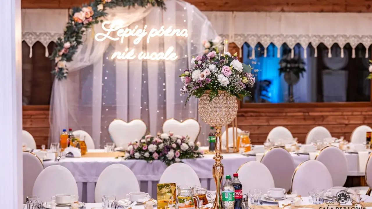 Eleganckie nakrycia stołów i kwiaty tworzą atmosferę kameralnego wesela. Neonowy napis "Lepiej późno niż wcale" dodaje uroku.