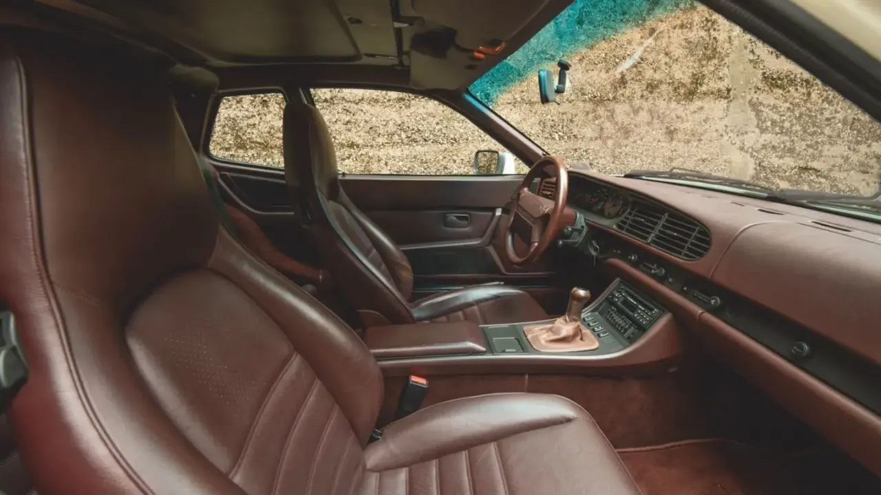 Das **Porsche 944 Interieur** mit braunen Ledersitzen und Armaturenbrett. Ein Blick auf das Lenkrad, den Schalthebel und das Radio.