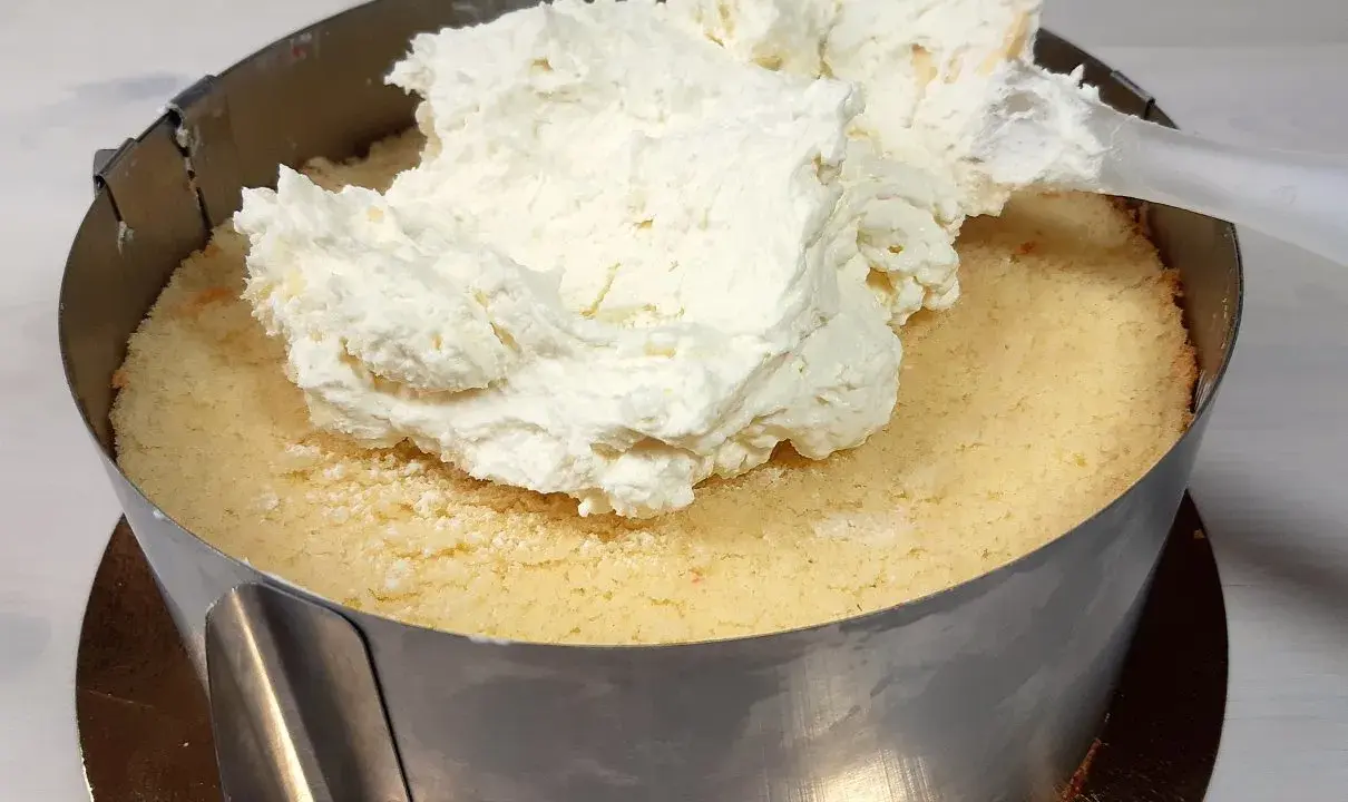 Nakładanie puszystego kremu mascarpone na biszkopt w tortownicy.