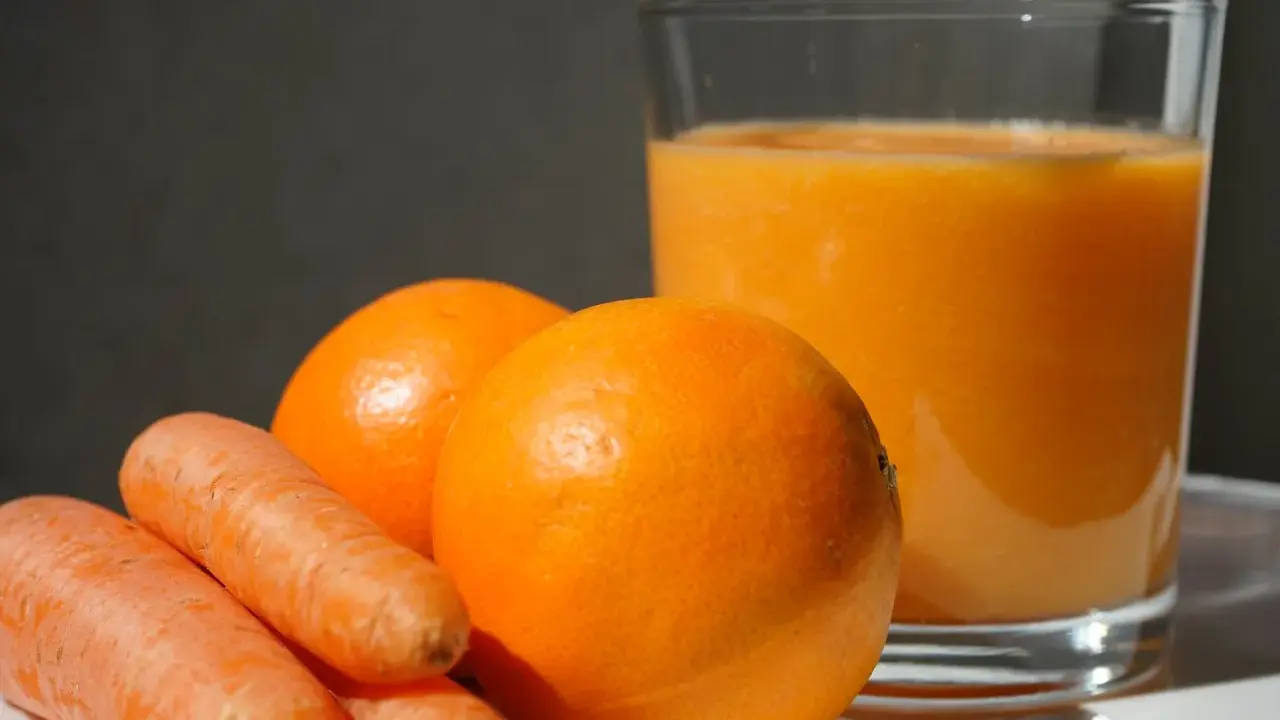 Pomarańcze i marchewki obok szklanki soku. Idealne składniki na zdrową dieta warzywno owocowa.