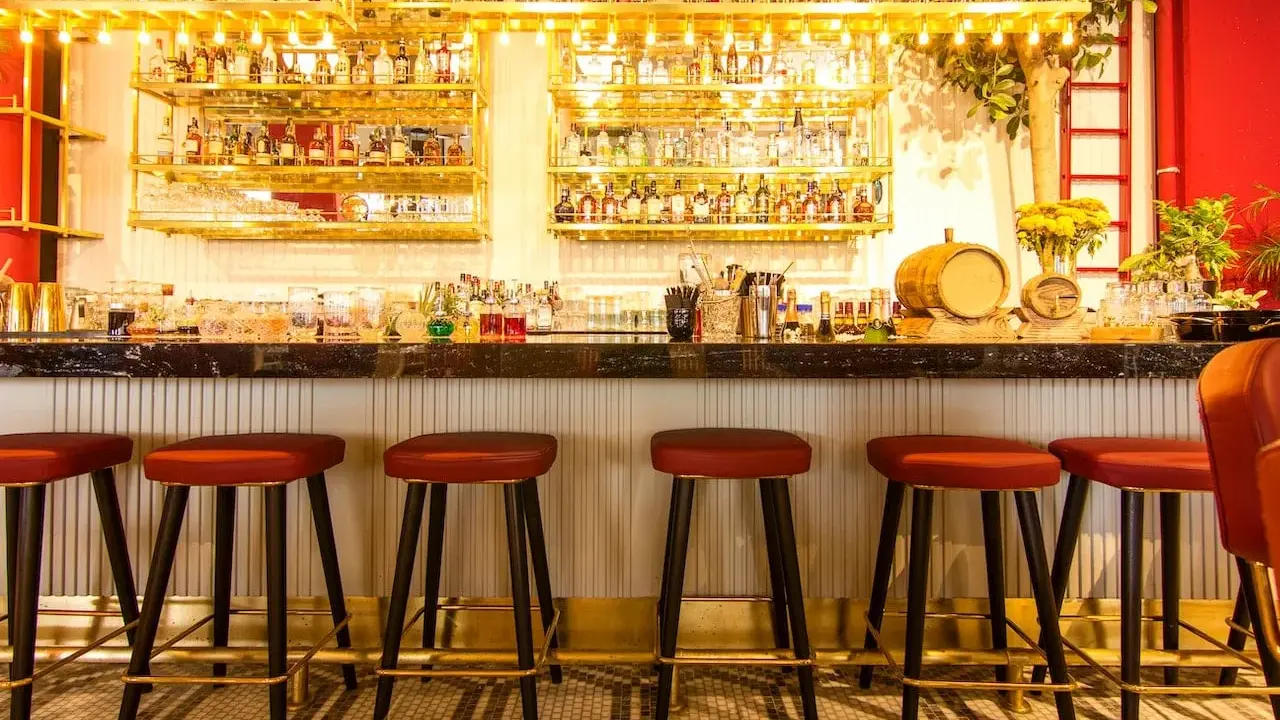 Bar con botellas doradas y taburetes rojos. Ideas para decorar un bar con poco dinero: ¡la iluminación y los detalles marcan la diferencia!