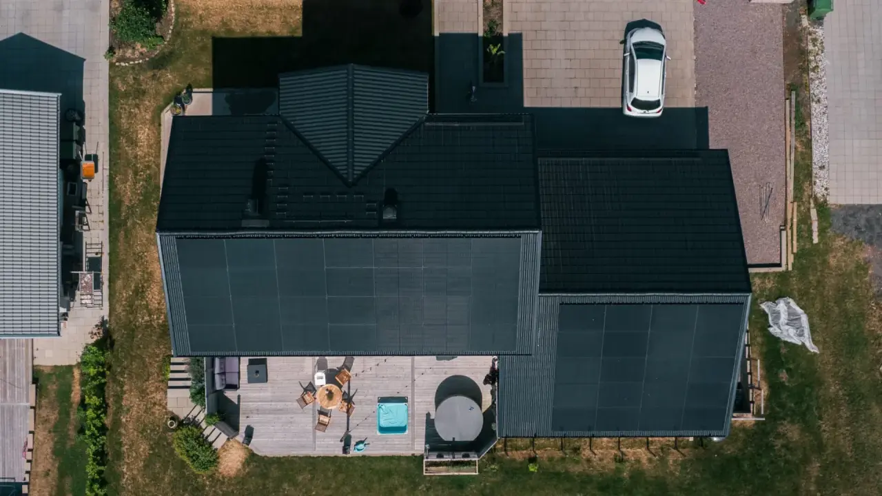 Villa med solceller och ett modernt batterilager. Uteplats med spabad och utemöbler. En vit bil parkerad på uppfarten.