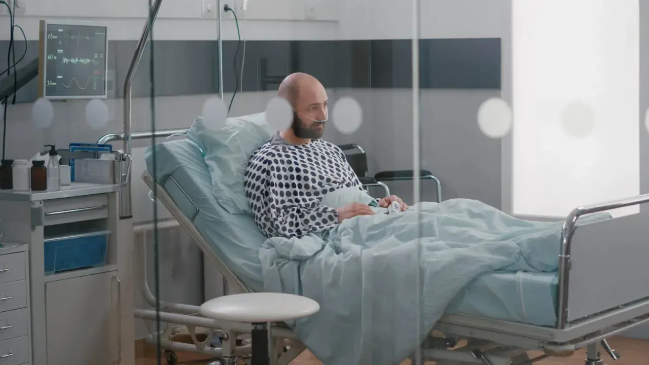 Mężczyzna w szpitalnym łóżku, z tlenem w nosie, czeka na wypis. Jego pobyt w szpitalu a zwolnienie lekarskie to teraz kluczowe kwestie.