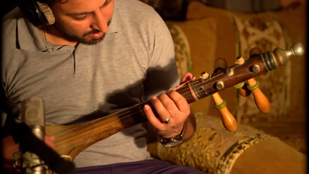 Un homme joue d'un instrument à corde marocain, un guembri, devant un microphone.