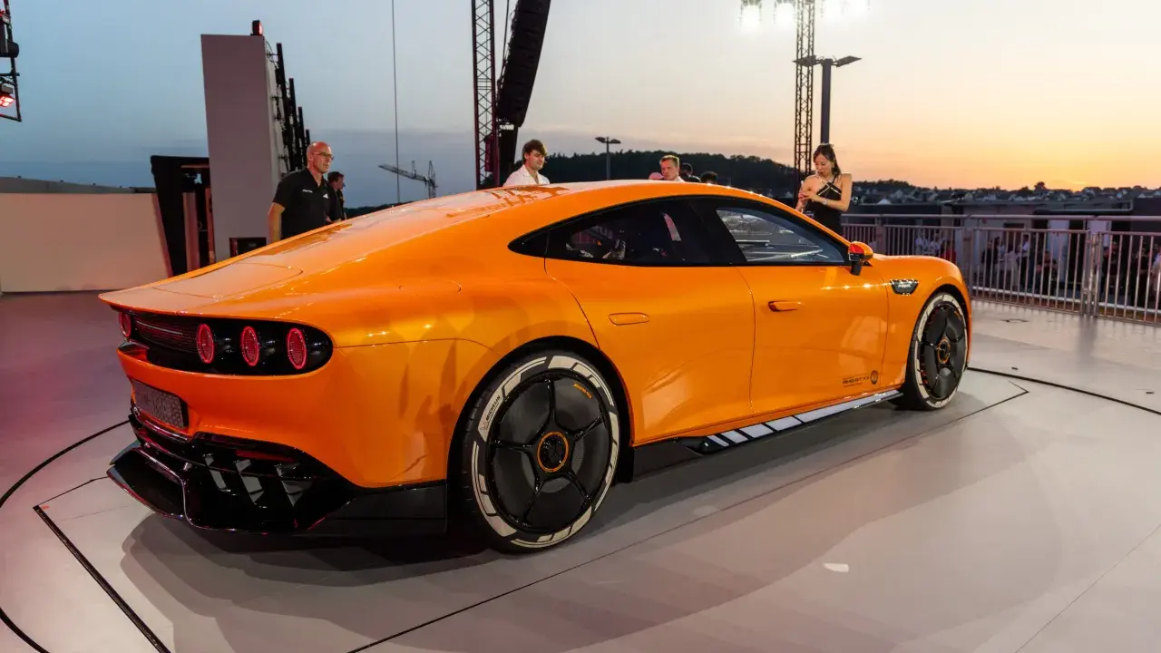 Ein leuchtend oranger AMG GT XX steht auf einer Bühne, beleuchtet vom Abendhimmel.
