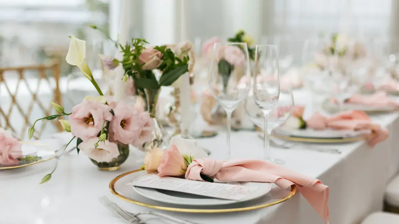 En vacker fest dukning med rosa blommor, glas och menyer.