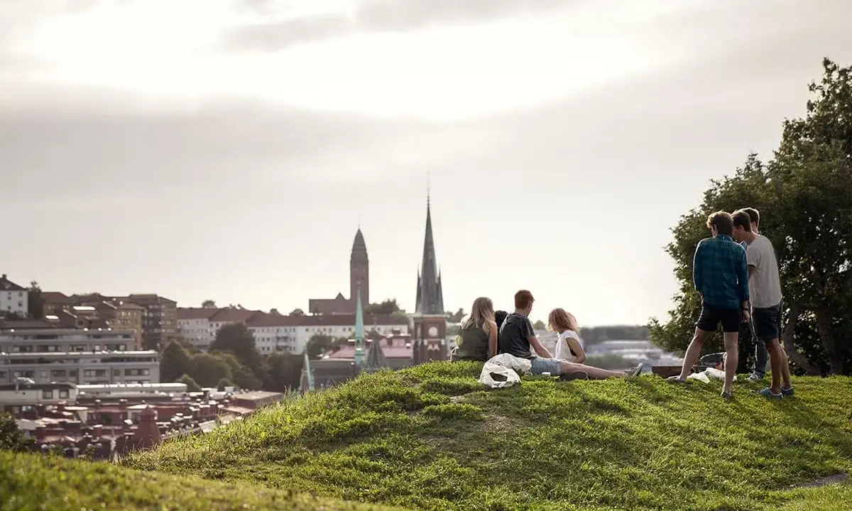 Vänner njuter av utsikten över Haga, Göteborg. En grupp unga människor sitter på en gräskulle med staden i bakgrunden.