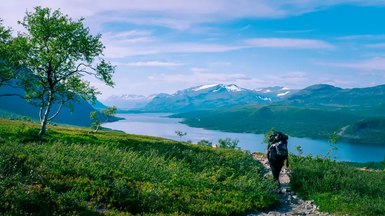 Vandra i Norrland med storslagen utsikt över sjö och snöklädda berg. En ensam vandrare med ryggsäck går på en stenstig.