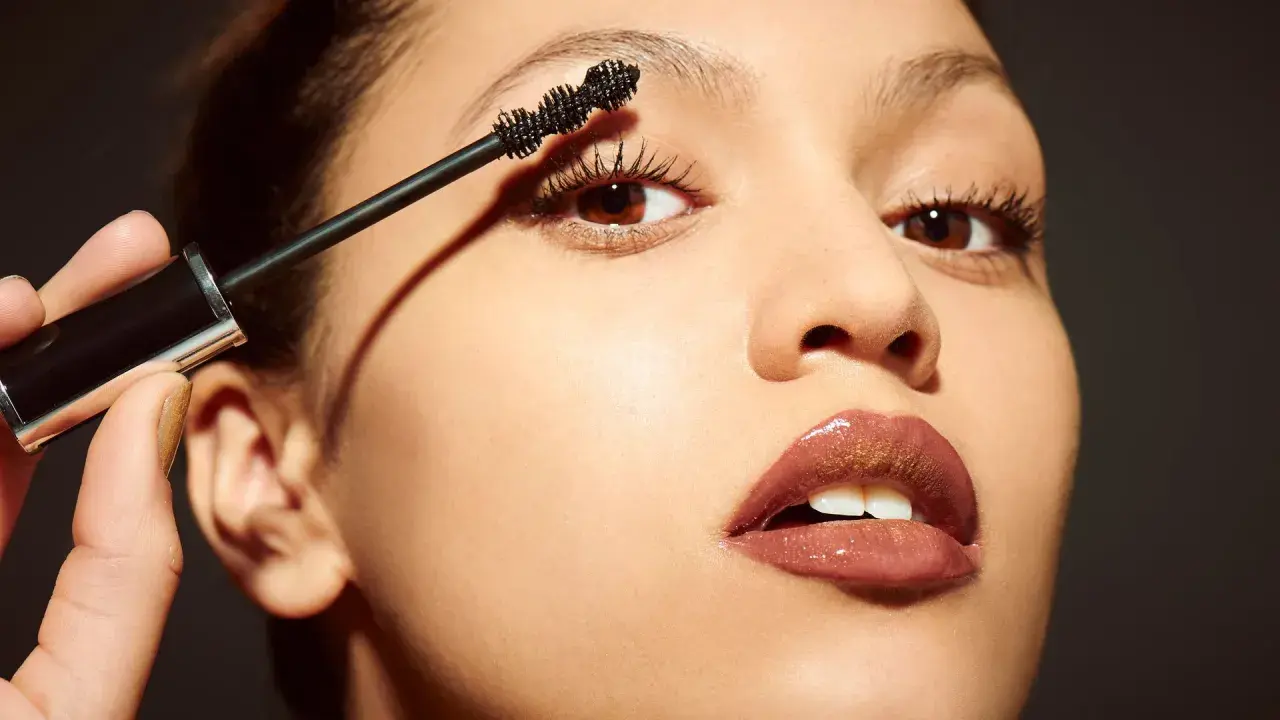 Una mano aplica máscara de pestañas a unos ojos pequeños, resaltando su belleza natural.