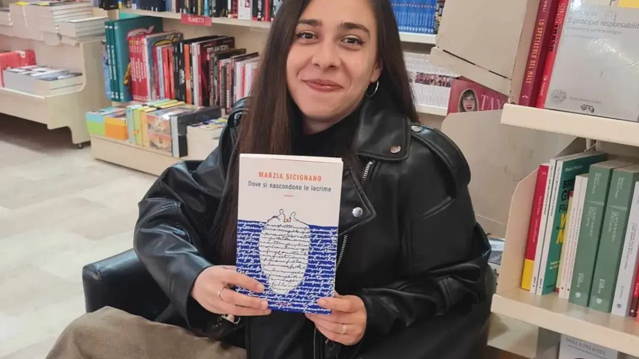 Una giovane donna sorride in libreria, tenendo in mano il libro "Dove si nascondono le lacrime".