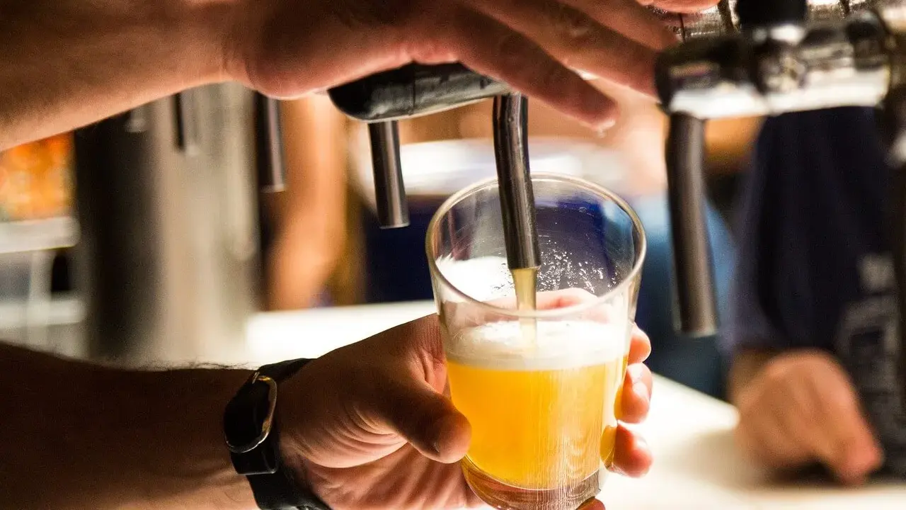 Ręka nalewa złociste piwo do szklanki. Czy alkoholik może pić piwo bezalkoholowe? To pytanie, na które odpowiedź zależy od indywidualnej sytuacji.
