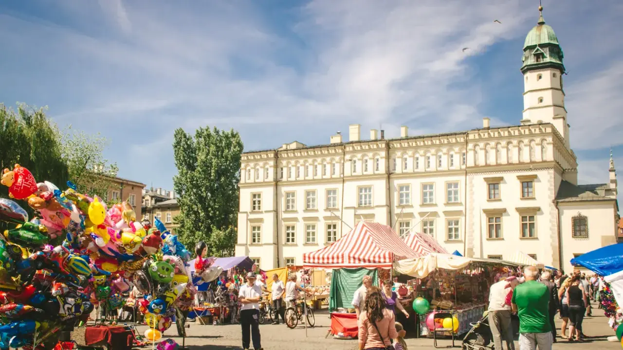 Kolorowy jarmark na rynku na Kazimierzu w Krakowie. Balony, stragany z pamiątkami i ludzie spacerujący pod jasnym niebem.