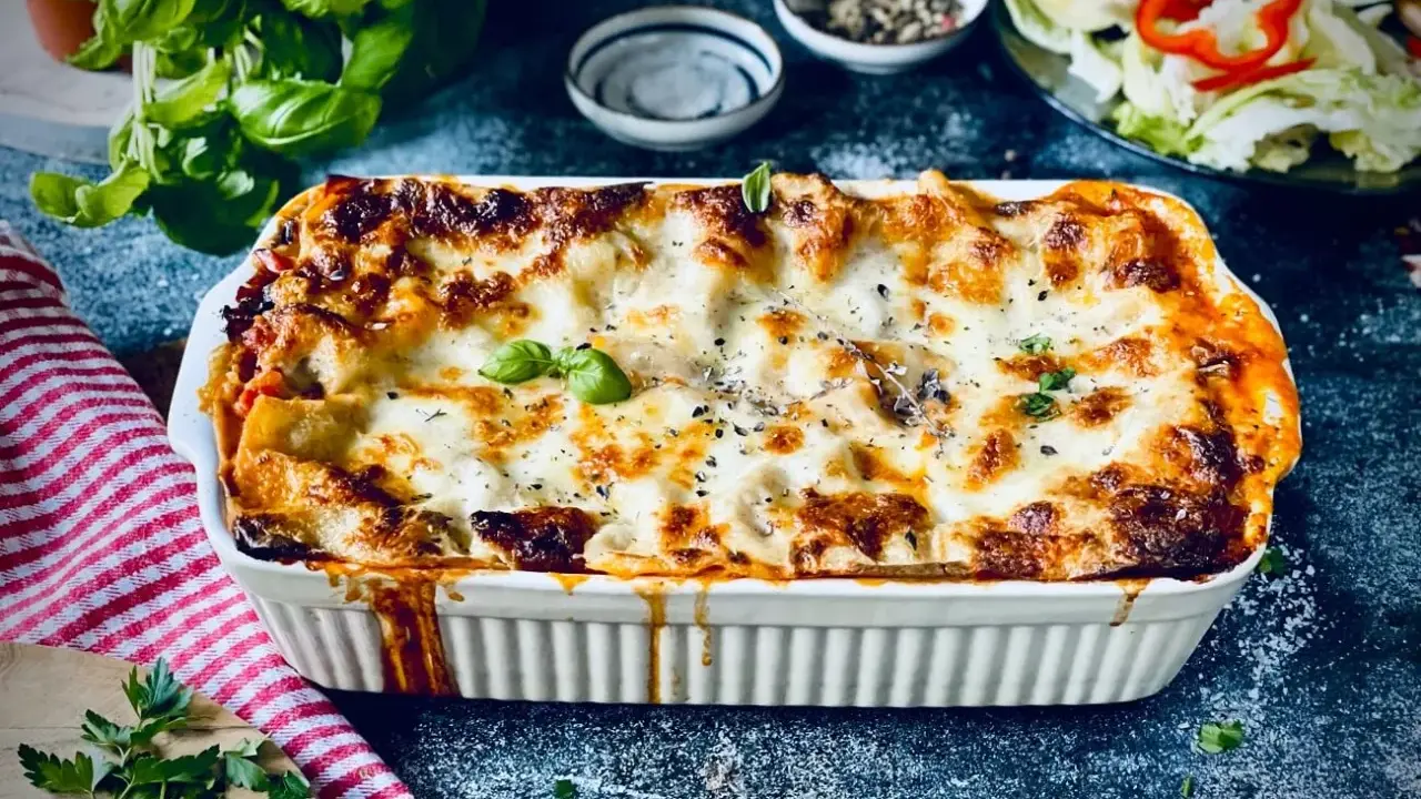 Herzhafte vegetarische Lasagne mit geschmolzenem Käse und frischem Basilikum, serviert in einer weißen Auflaufform.