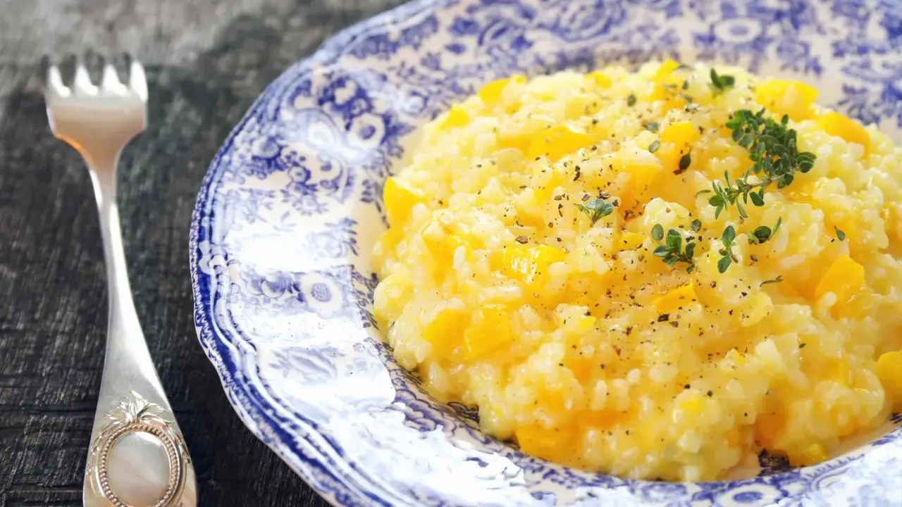 Pyszny, kremowy ryż do risotto z kawałkami dyni, posypany świeżym tymiankiem i pieprzem. Obok leży elegancki widelec.