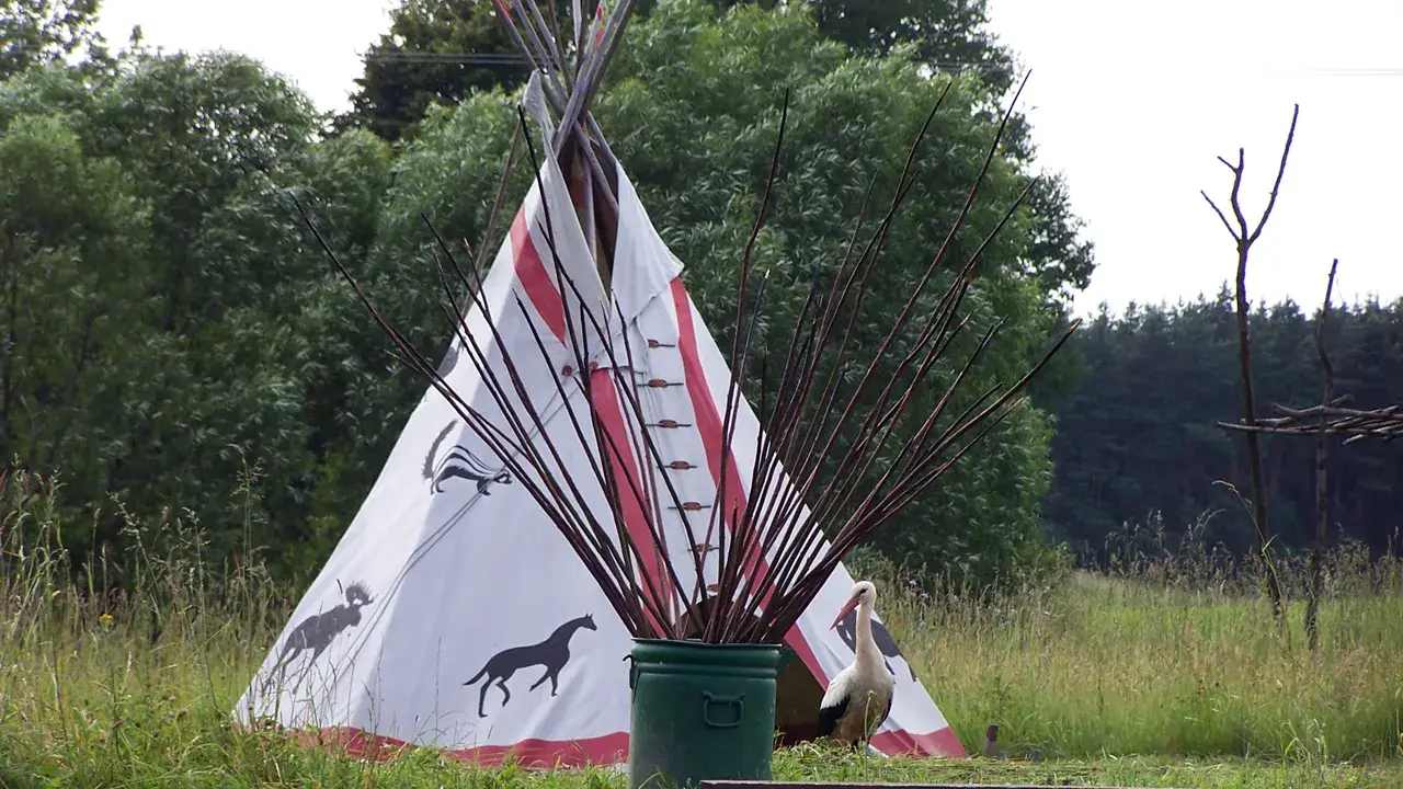 Wioska indiańska na Mazurach z tipi ozdobionym zwierzętami, bocianem i łukami.