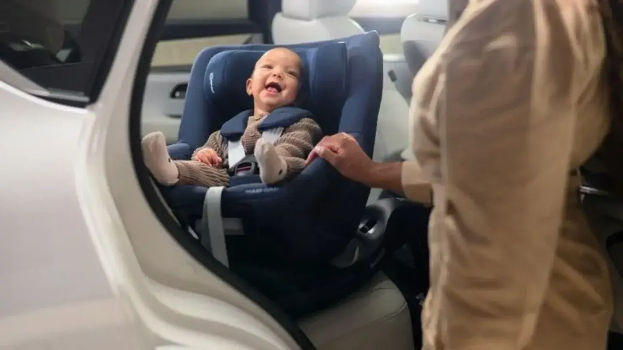 Bebé sonriente en un maxicosi azul, listo para aprender como colocar el maxicosi en el coche.