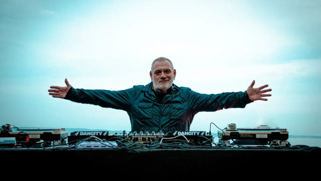 DJ Ralf, un vero patrimonio della musica elettronica, con le braccia aperte davanti alla sua consolle, pronto a far ballare il mondo.
